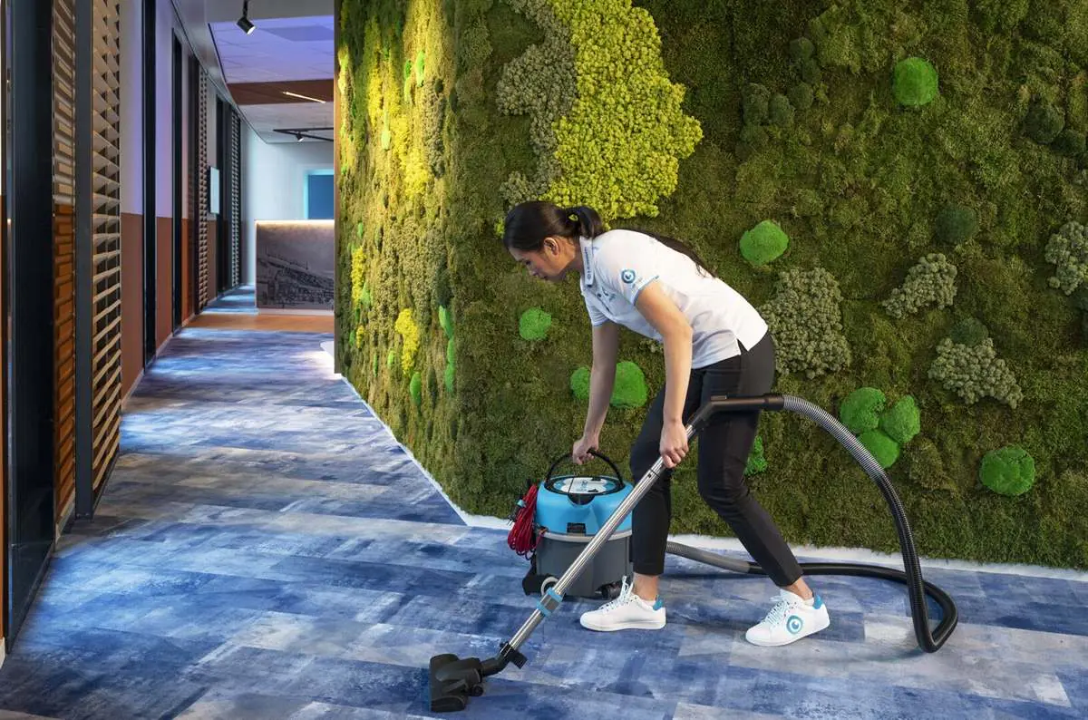 Une agente aspire la moquette d'un couloir de bureaux avec un aspirateur i-vac
